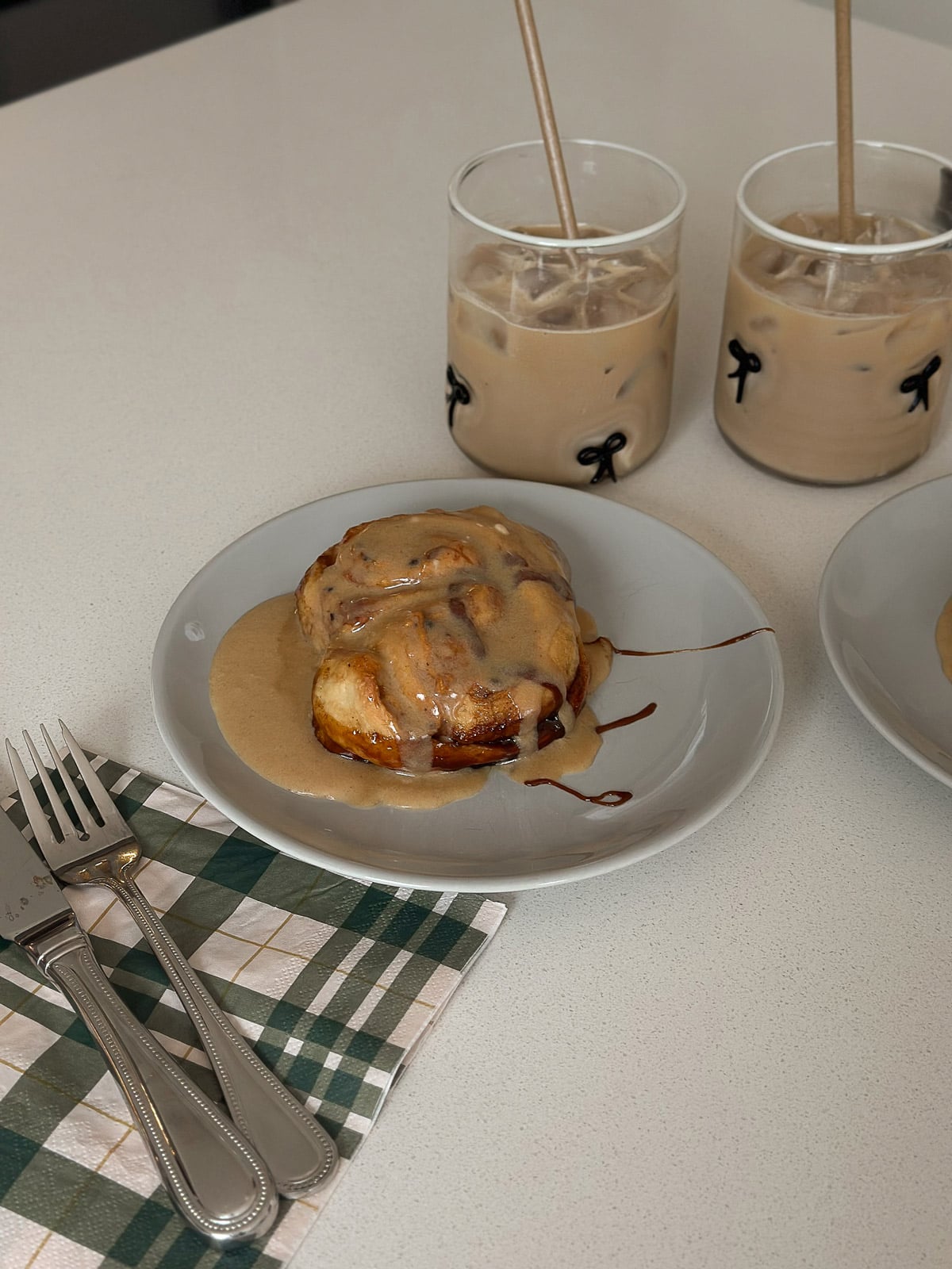 Close-up of a frosted cinnamon roll on a plate with iced coffee in the background