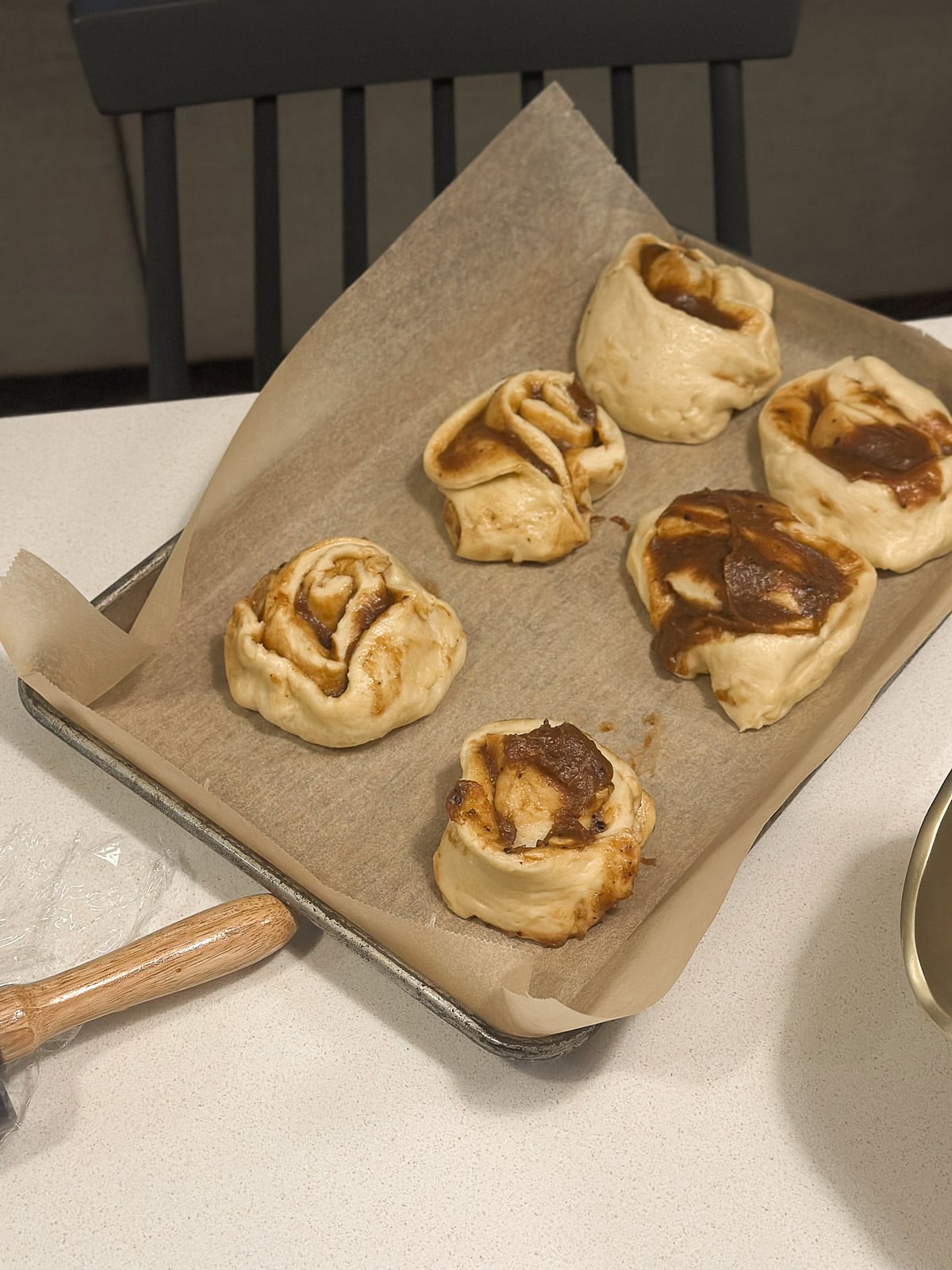Messy uneven cinnamon rolls on parchment paper in a baking sheet with a rolling pin
