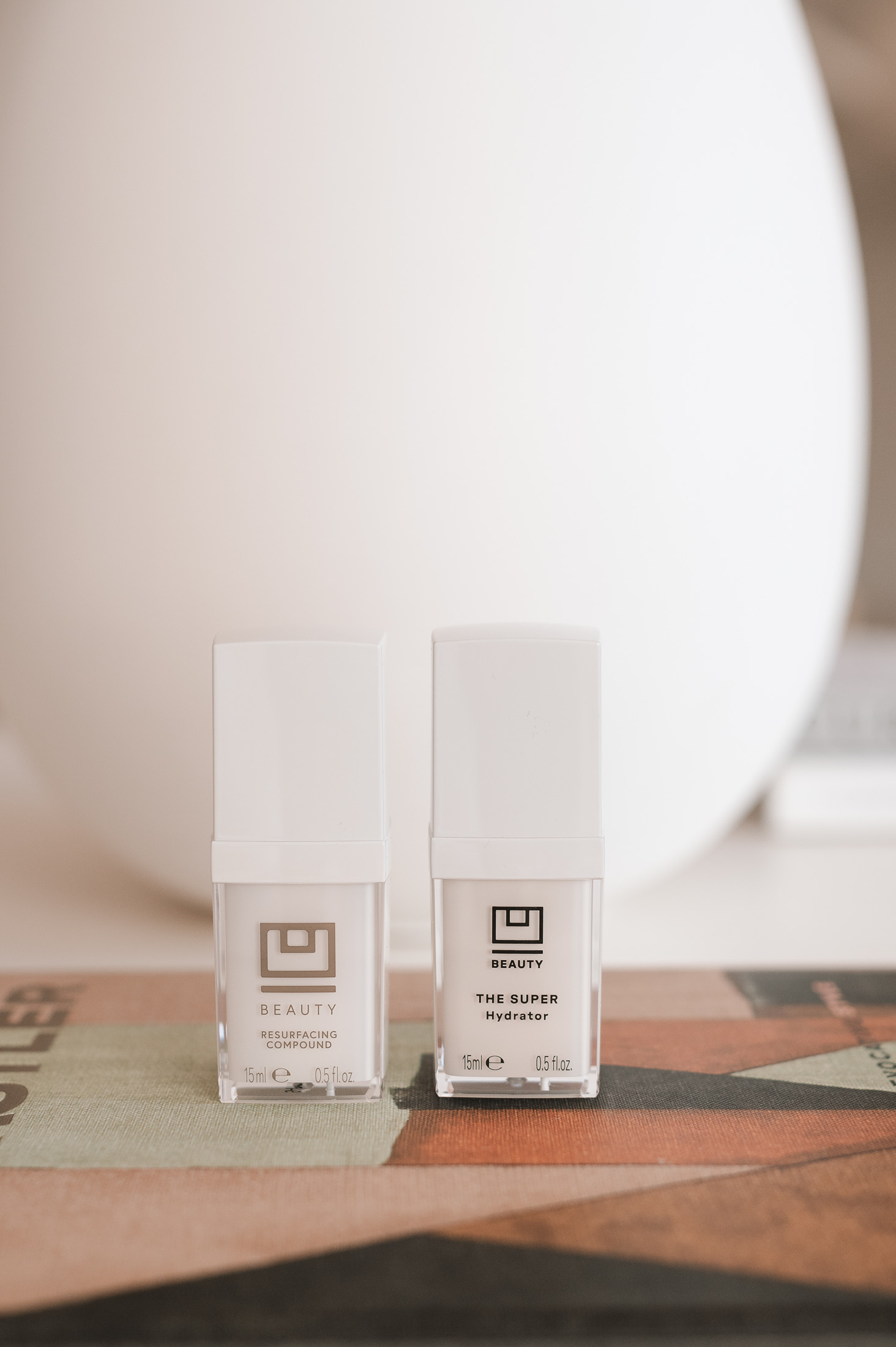 U Beauty Resurfacing Compound and Super Hydrator skincare bottles on a colorful book