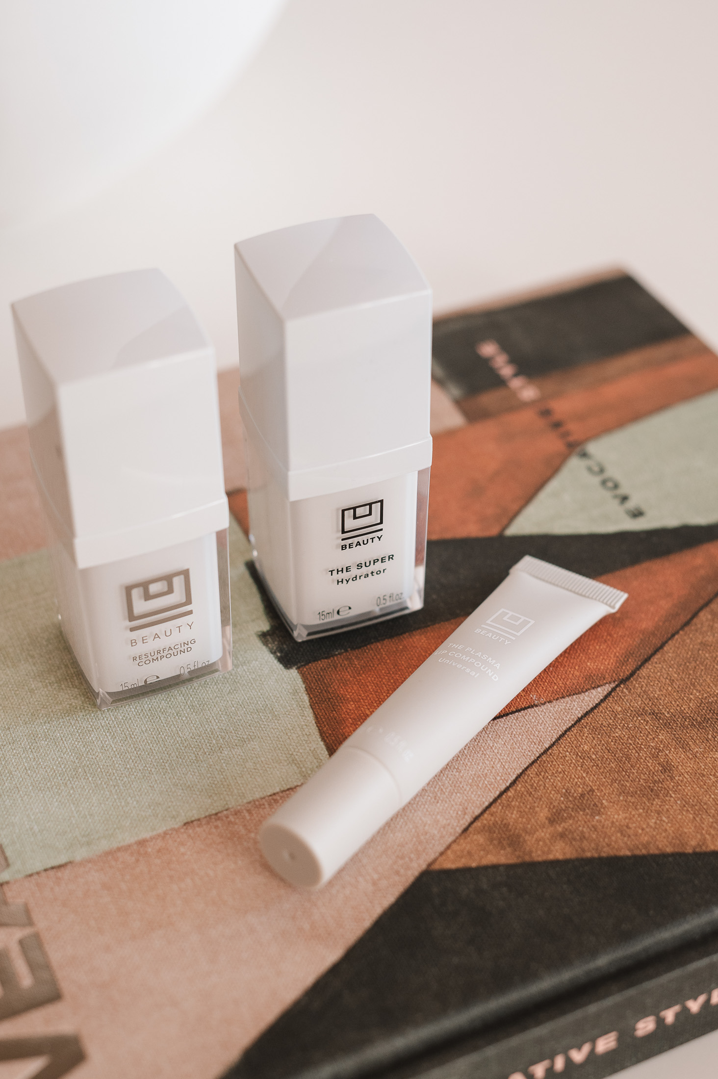 U Beauty Resurfacing Compound and Super Hydrator skincare bottles and Lip Plasma tube on a colorful Kelly Wearstler book