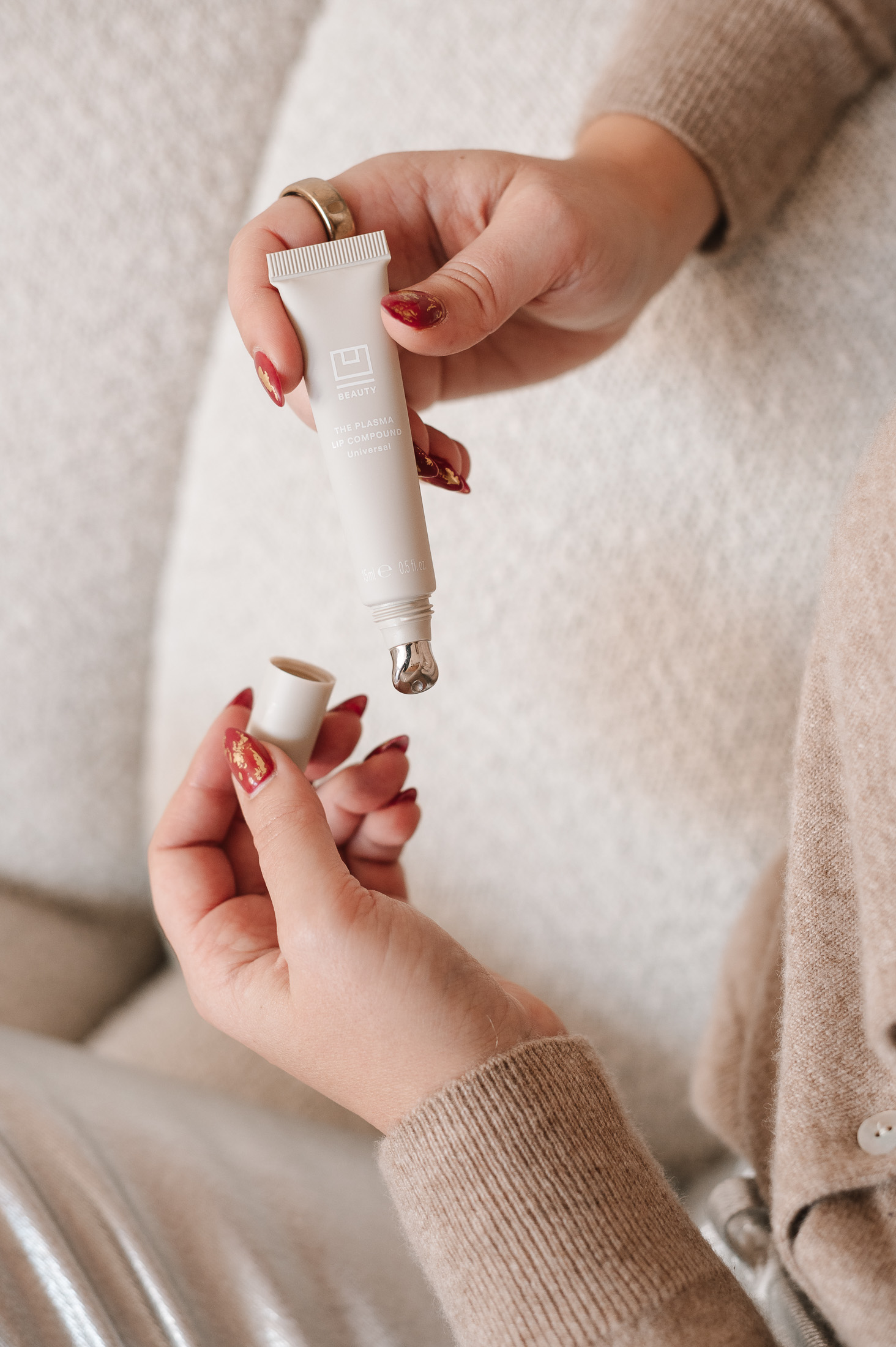 Close-up of metal applicator tip on U Beauty Plasma Lip Compound in front of boucle couch